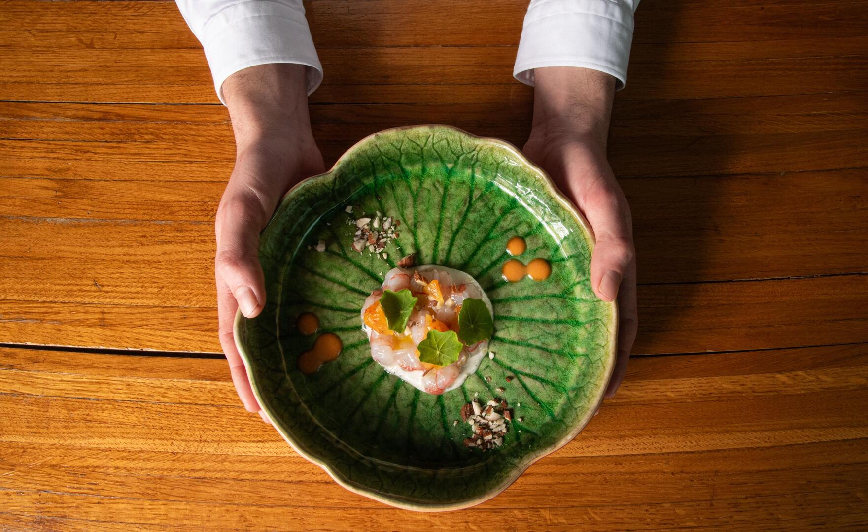 A green plate featuring a shrimp dish held in hands.