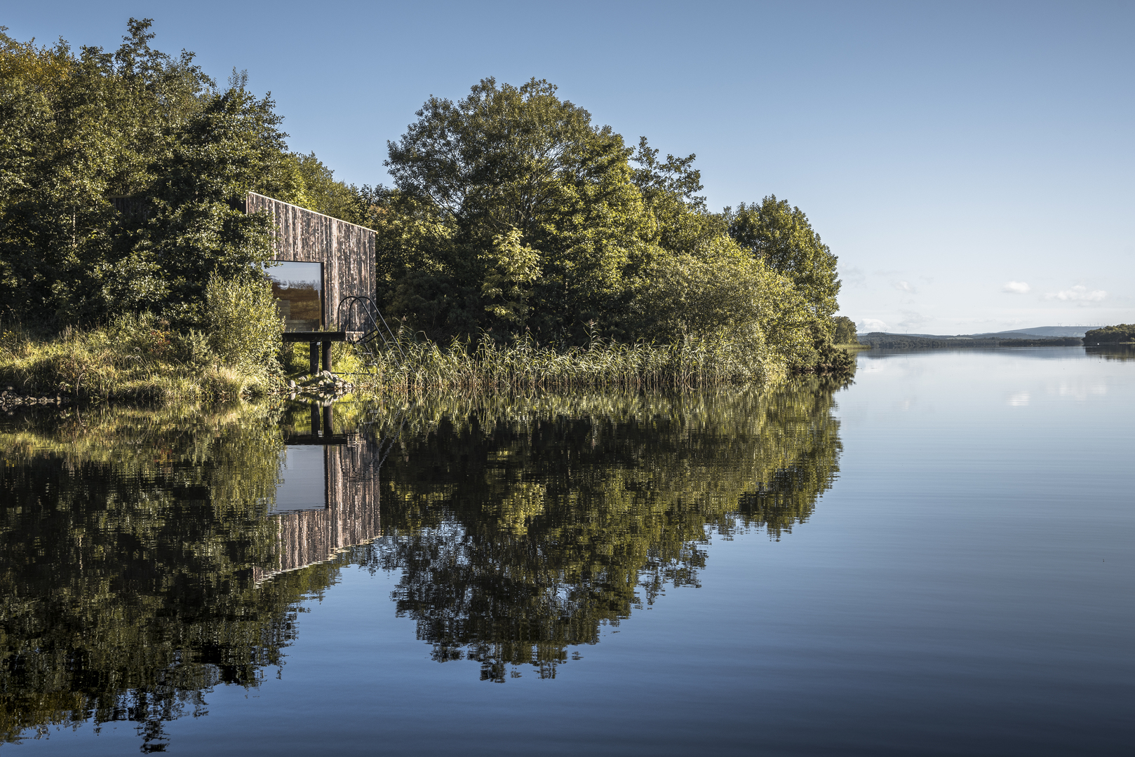 Lake cabin reflected in calm water.