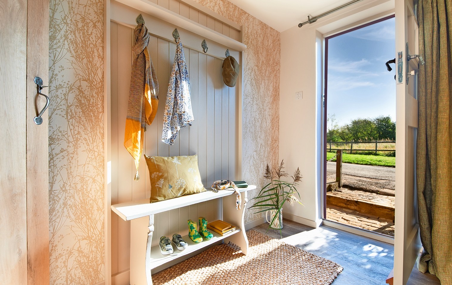 Hallway with bench, coat rack, and open door to a sunny yard.