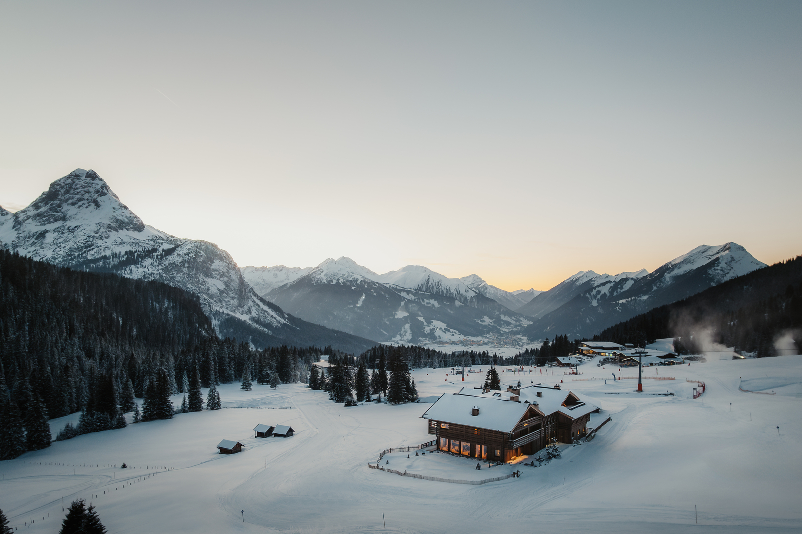 Aerial view of a luxury hotel in a snowy mountain valley at sunset.