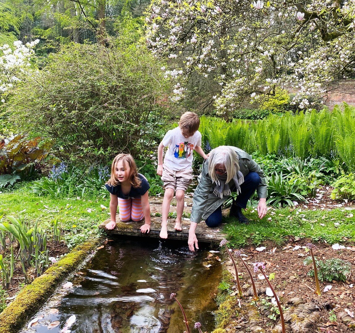 Two children and an adult playing in a stream in a garden.