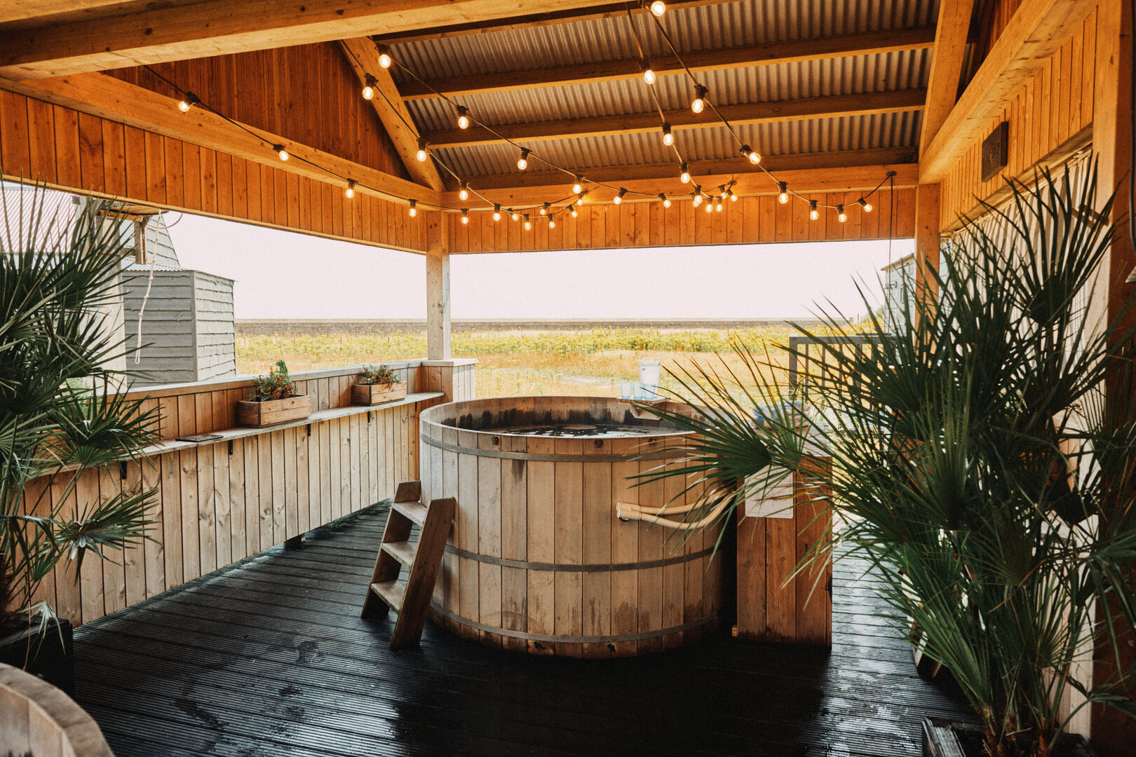 Wooden hot tub on a deck with string lights.