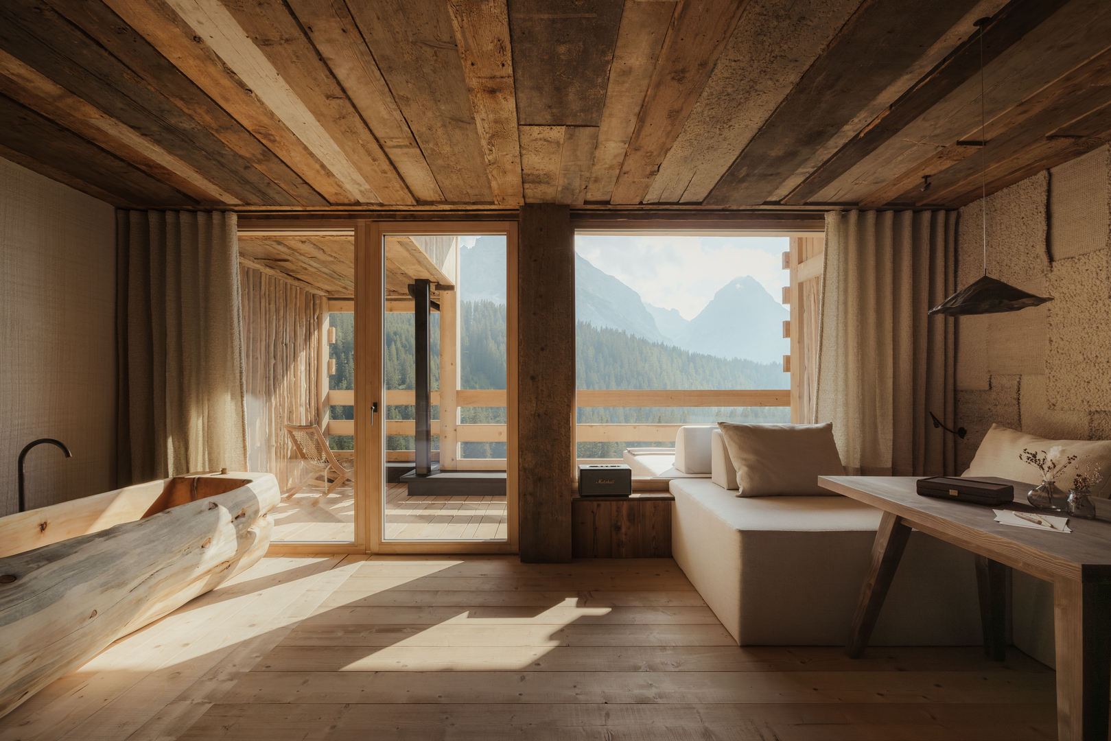 Interior view of a luxury hotel room with a wooden bathtub, seating area, and mountain view.