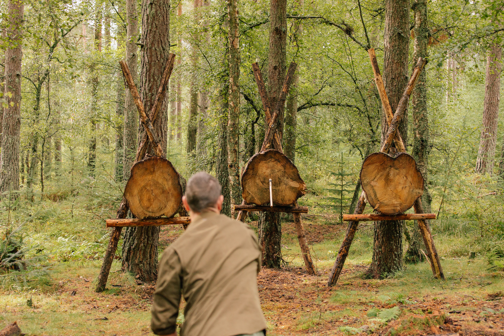 Person throwing axe at three wooden targets in a forest.